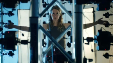 Elizabeth Holmes em uma estrutura metálica cercada por equipamentos de filmagem no filme You Can See Everything (2026).