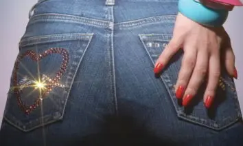 Parte traseira de uma calça jeans decorada com strass em forma de coração, mão com unhas vermelhas e pulseiras coloridas, imagem promocional do filme de terror cômico Slaxx (2020).