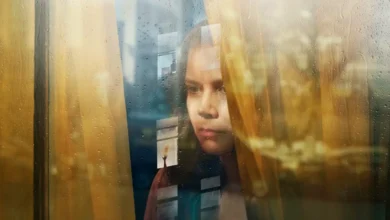Amy Adams em cena do thriller psicológico A Mulher na Janela (2021), observando pela janela em meio a reflexos e clima de suspense.