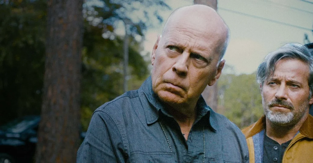 american siege sinopse Bruce Willis com expressão séria em cena de American Siege (2022), ao lado de outro personagem, em uma floresta ao fundo
