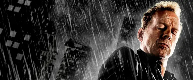 Bruce Willis em Sin City: A Cidade do Pecado 2005, personagem em cena sob forte chuva, com expressão séria e atmosfera sombria.