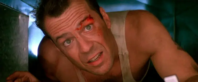 Bruce Willis em Duro de Matar (1988), expressão de esforço e determinação em cena icônica do filme de ação.