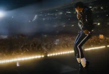 Jaafar Jackson caracterizado como Michael Jackson em cena do filme Michael, dançando em palco iluminado diante de multidão em estádio lotado