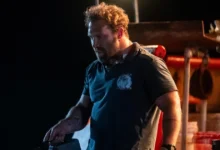 Jai Courtney em cena tensa à noite no filme Animais Perigosos (2025), usando camiseta escura em um barco pesqueiro iluminado por luz artificial.