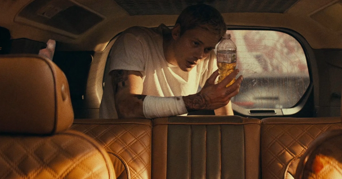 10 filmes claustrofobicos para ver antes de confinado Cena do filme Confinado, um dos novos filmes claustrofóbicos, mostra o personagem de Bill Skarsgård dentro de um carro apertado e fechado, ferido e segurando uma garrafa com líquido amarelo, transmitindo tensão e isolamento.