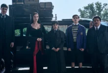 Cena da segunda temporada de Wandinha com Joonas Suotamo, Catherine Zeta-Jones, Jenna Ortega, Isaac Ordonez e Luis Guzmán posando em frente a um carro antigo.