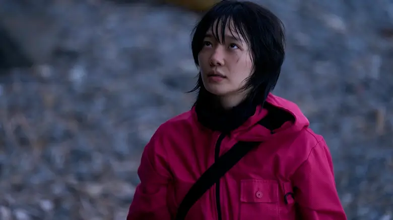 estreia terceira temporada round 6 Park Gyuyoung em cena de Round 6, usando macacão rosa em ambiente rochoso