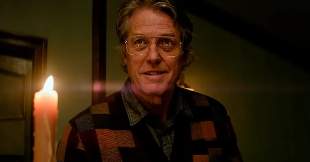 Hugh Grant caracterizado como Mr. Reed em Herege (2024), sorrindo em uma cena à luz de velas, com expressão enigmática e figurino retrô.