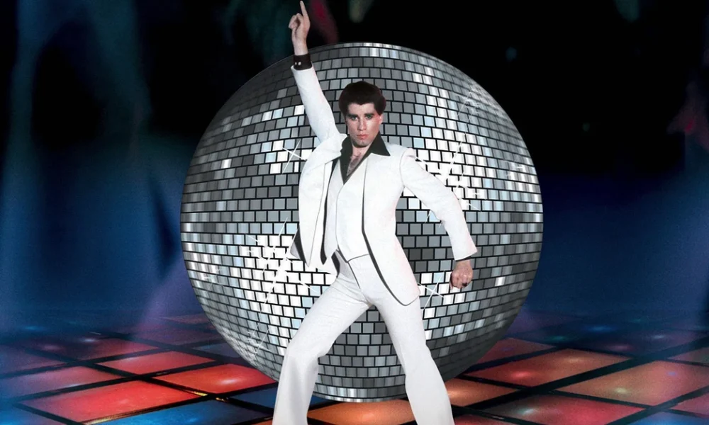 Cena icônica do filme Os Embalos de Sábado à Noite (1977), com John Travolta dançando sob luzes coloridas e globo espelhado — imagem destaque da matéria “As 5 músicas mais utilizadas em trilhas de filmes”