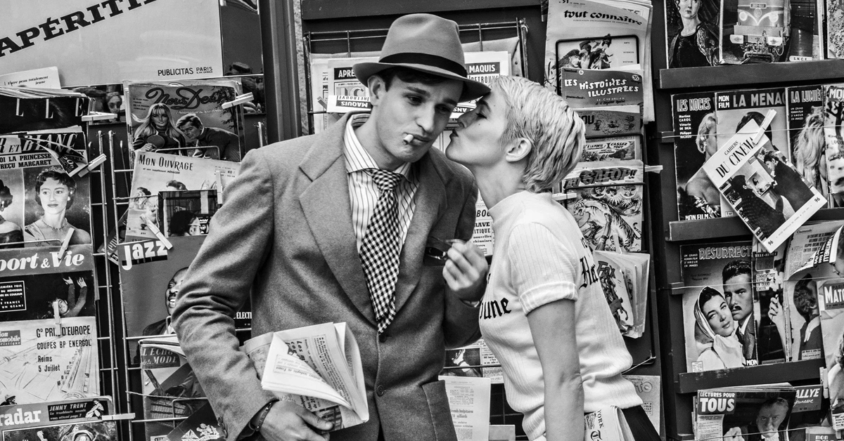 nouvelle vague trailer Cena do filme Nouvelle Vague, dirigido por Richard Linklater, com Zoey Deutch e Aubry Dullin. Os personagens estão em frente a uma banca de revistas vintage, com figurinos retrô dos anos 60, em clima de romance e nostalgia.