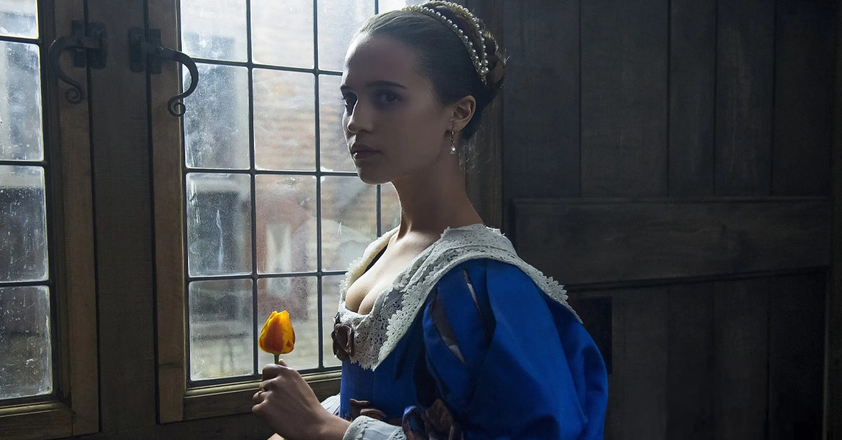novo trailer de amor e tulipas Cena do filme Amor e Tulipas (2017) com Alicia Vikander segurando uma tulipa amarela enquanto olha pela janela em um ambiente com luz suave.