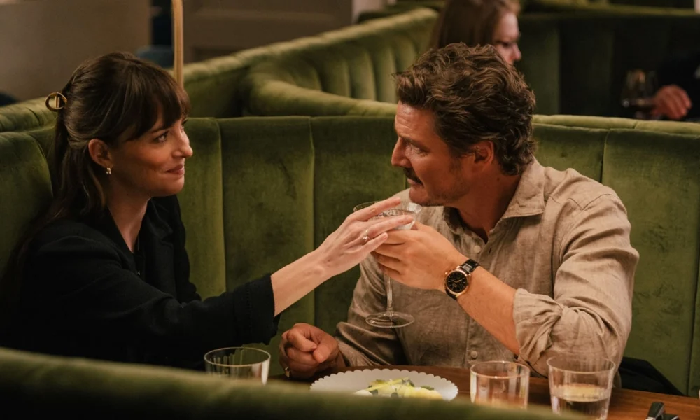 Cena do filme Materialists (2025) mostra Dakota Johnson e Pedro Pascal brindando em um restaurante elegante; à esquerda, Johnson sorri enquanto segura uma taça, e à direita, Pascal retribui o gesto com olhar carinhoso. Filme também conta com Chris Evans no elenco.