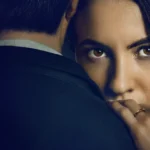 Imagem promocional do filme "O Jogo da Viúva" (2025), da Netflix, com Ivana Baquero encarando a câmera enquanto abraça o personagem de Tristán Ulloa.