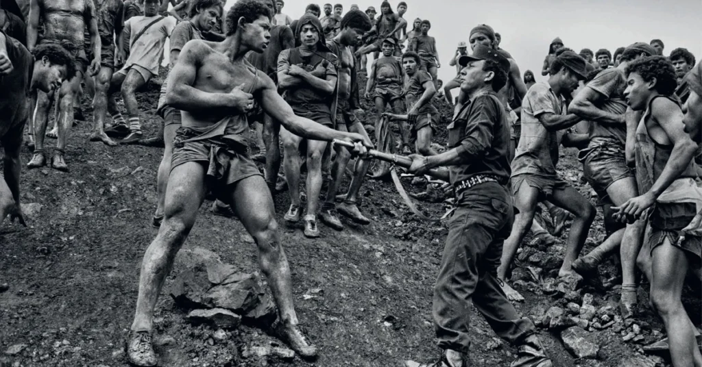 Garimpeiros cobertos de lama disputam uma ferramenta em uma encosta íngreme, em cena registrada por Sebastião Salgado no documentário O Sal da Terra.