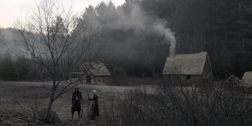 oracamento a Locação do filme A Bruxa (2015), com casas de madeira e vegetação ao fundo, filmada na remota região de Kiosk, em Ontário, Canadá, cenário que reforça a atmosfera sombria e isolada da história