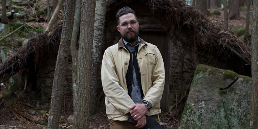 robert eggers Robert Eggers em frente a uma cabana na floresta durante os bastidores do filme A Bruxa (2015), filme de terror aclamado por sua atmosfera sombria e realismo histórico.