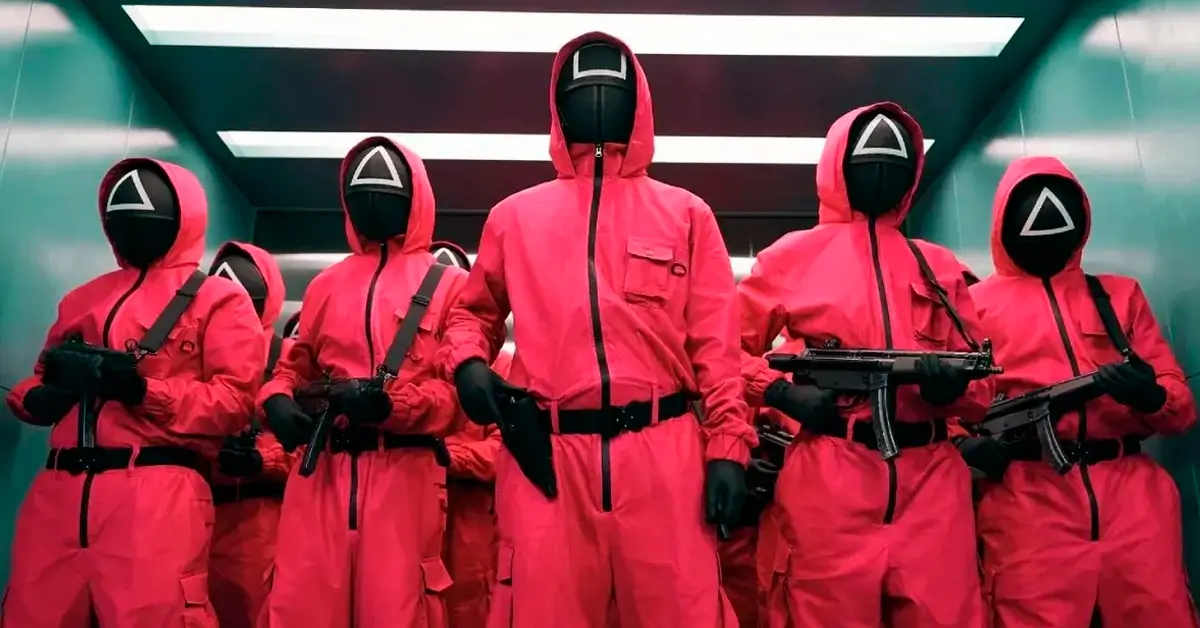 Guardiões mascarados de vermelho armados em cena de Round 6, série da Netflix.