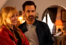 Colin Farrell e Margot Robbie sorrindo em cena do trailer de A Grande Viagem da Sua Vida, com ambiente interno iluminado ao fundo.