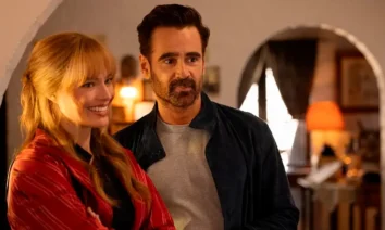 Colin Farrell e Margot Robbie sorrindo em cena do trailer de A Grande Viagem da Sua Vida, com ambiente interno iluminado ao fundo.