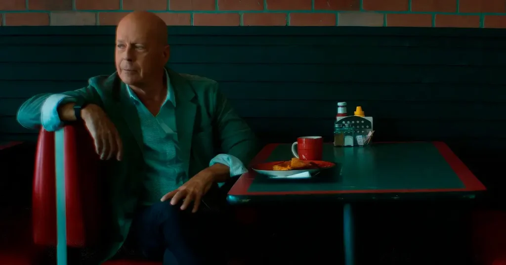 bruce willis assassin Bruce Willis sentado sozinho em uma lanchonete no filme Assassin (2023), olhando para o lado com expressão séria