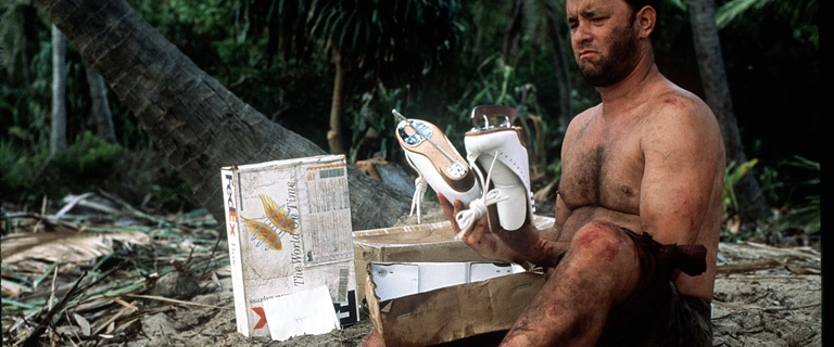 Tom Hanks como Chuck Noland abrindo pacotes da FedEx em cena do filme Náufrago (2000), segurando um par de patins de gelo.
