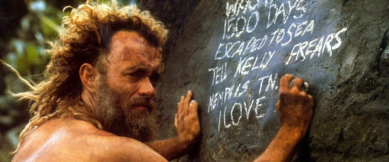 Tom Hanks como Chuck Noland escreve mensagem de despedida em uma pedra em cena dramática do filme Náufrago (2000).