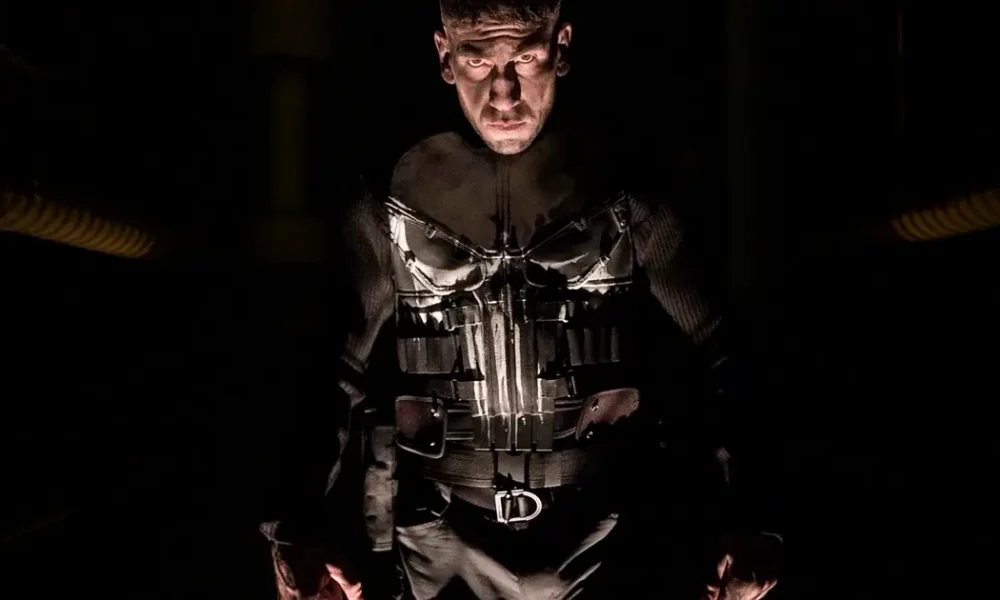 o justiceiro serie teaser Jon Bernthal como Frank Castle, O Justiceiro, com traje preto e caveira branca em ambiente escuro e dramático.