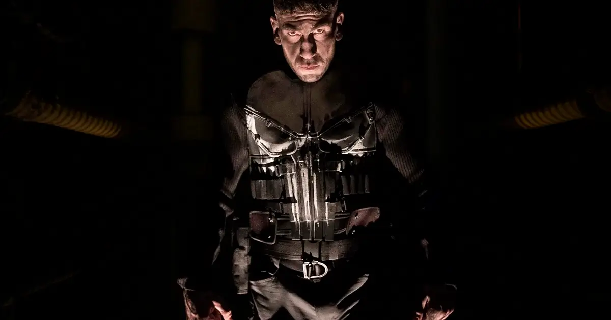 Jon Bernthal como Frank Castle, O Justiceiro, com traje preto e caveira branca em ambiente escuro e dramático.