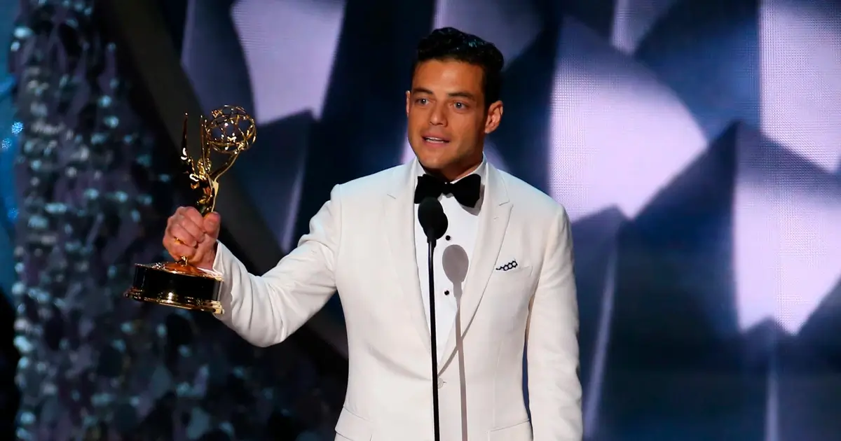 Rami Malek recebe o Emmy de Melhor Ator por Mr. Robot Rami Malek com smoking branco, segurando o troféu do Emmy de Melhor Ator em Série Dramática por sua atuação em Mr. Robot.