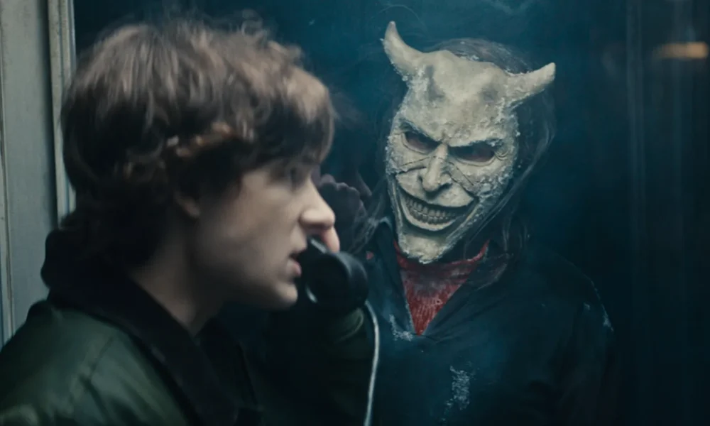 Cena do trailer de O Telefone Preto 2 mostra Finney (Mason Thames) em uma cabine telefônica, observado pelo sinistro vilão interpretado por Ethan Hawke, usando uma máscara demoníaca.