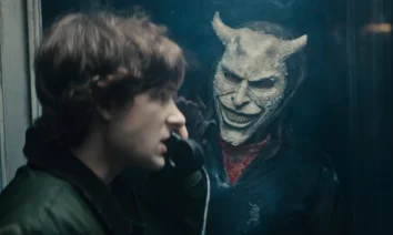 Cena do trailer de O Telefone Preto 2 mostra Finney (Mason Thames) em uma cabine telefônica, observado pelo sinistro vilão interpretado por Ethan Hawke, usando uma máscara demoníaca.