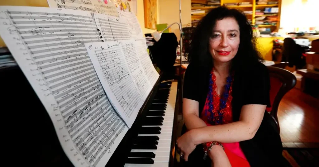 A compositora Elena Kats-Chernin ao lado de partituras em um piano.