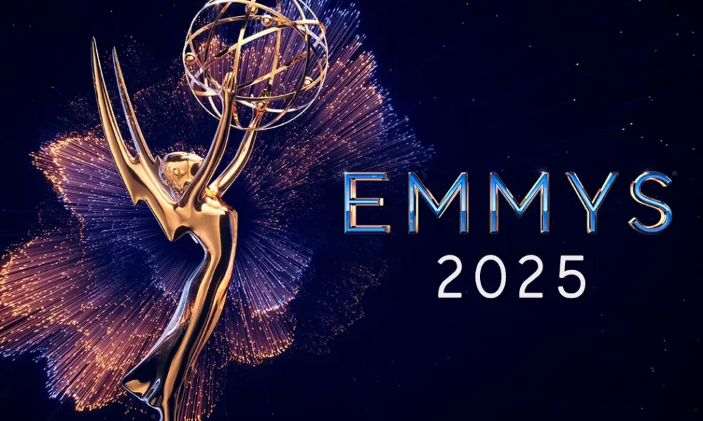 emmy 2025 indicados Uma imagem da estatueta dourada do Emmy, com braços estendidos segurando um globo, cercada por brilhos dourados e azuis que se assemelham a fogos de artifício ou explosões de luz. À direita, as palavras "EMMYS 2025" estão escritas em letras maiúsculas, com "EMMYS" em azul metálico e "2025" em branco. O fundo é um céu noturno escuro.