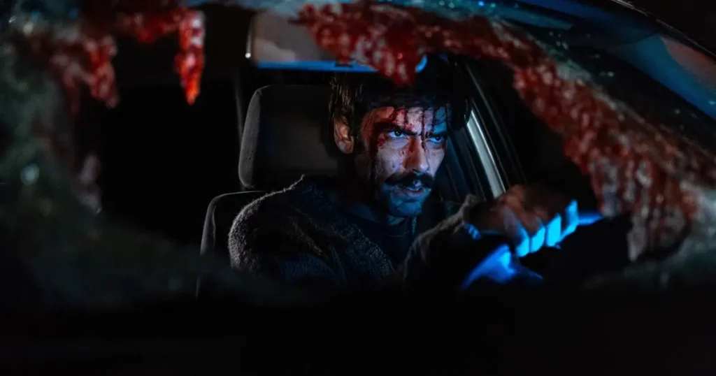 O ator Demián Salomón, coberto de sangue, dirige um carro com o para-brisa destruído em cena do filme O Mal que Nos Habita (2023).