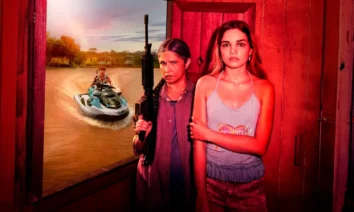 Cena promocional da minissérie Pssica da Netflix mostrando duas mulheres em primeiro plano - uma segurando uma arma automática e outra de braços cruzados - com um homem em jet ski ao fundo em águas lamacentas, ambientada em cenário amazônico com iluminação vermelha dramática