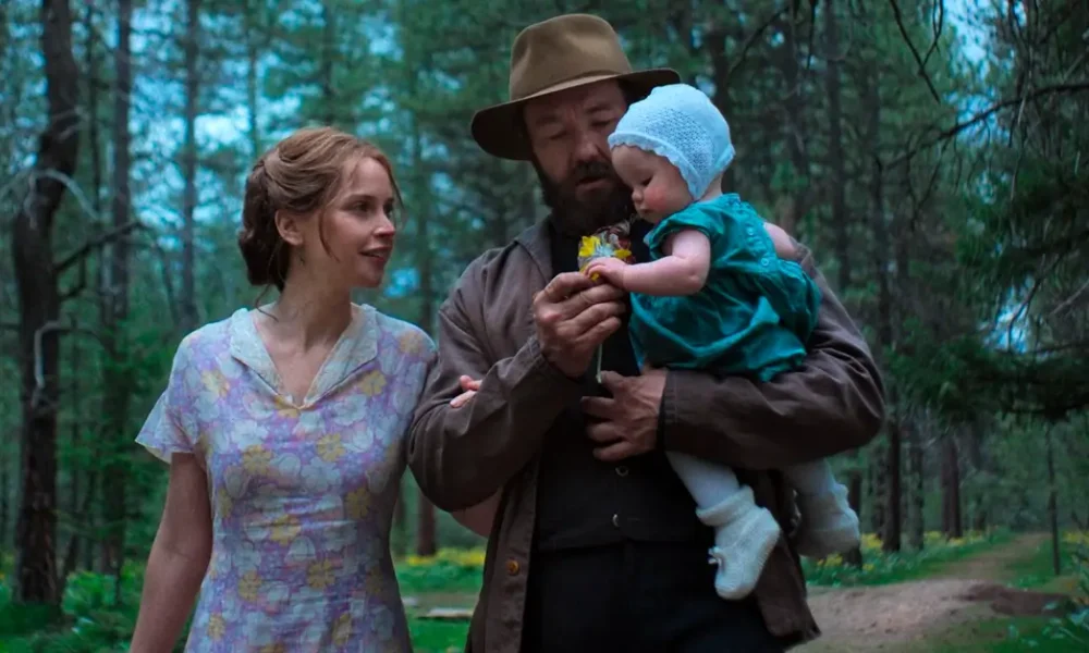 Joel Edgerton e Felicity Jones em cena do filme Sonhos de Trem, ele segurando um bebê em uma floresta