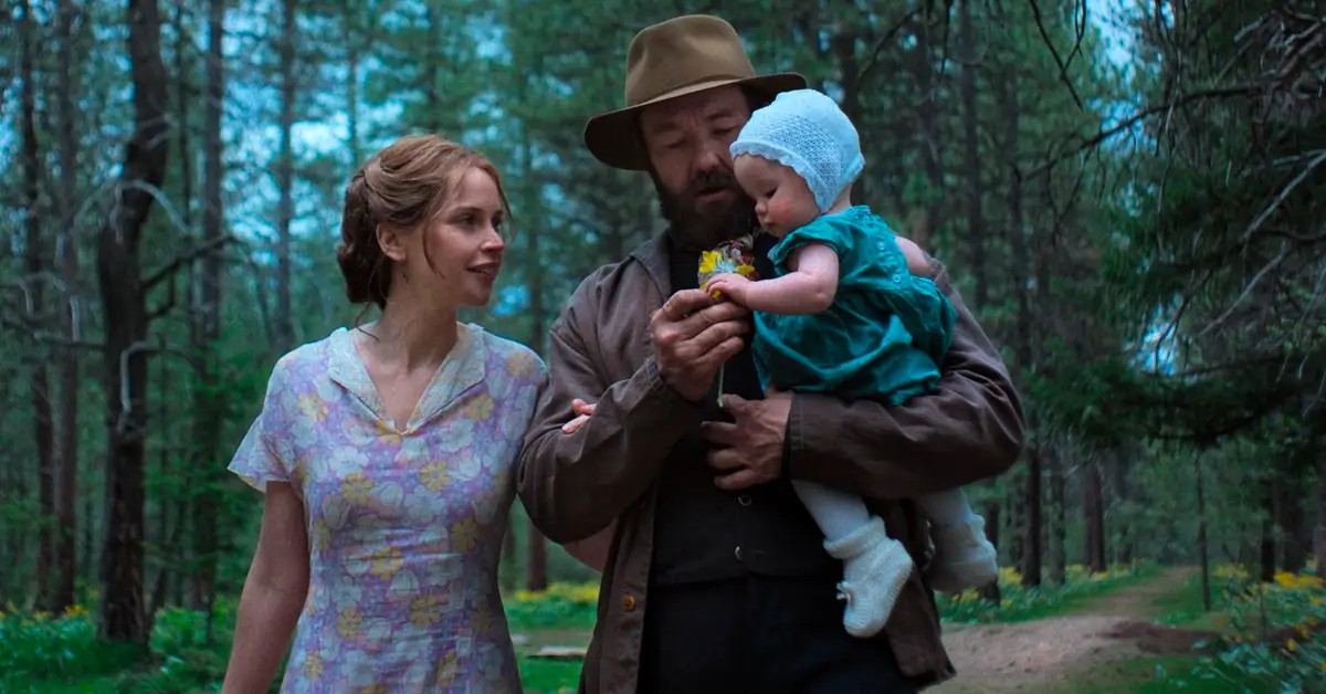 Joel Edgerton e Felicity Jones em cena do filme Sonhos de Trem, ele segurando um bebê em uma floresta