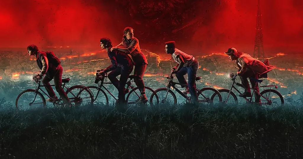 Elenco principal de Stranger Things 5 pedalando rumo ao caos, com o céu vermelho do Mundo Invertido ao fundo.