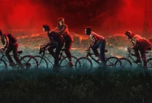Elenco principal de Stranger Things 5 pedalando rumo ao caos, com o céu vermelho do Mundo Invertido ao fundo.