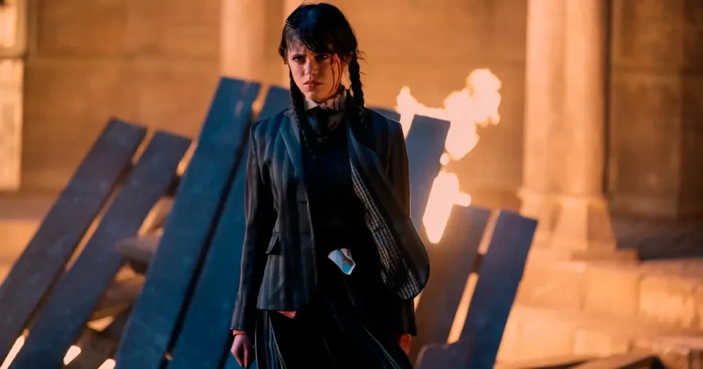 wandinha confrontando desgostos Wandinha enfrenta o inimigo no episódio final da primeira temporada, com fogo ao fundo