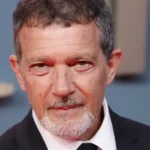 Antonio Banderas aos 65 anos em evento oficial, usando smoking preto e gravata, sorrindo para fotógrafos em tapete vermelho
