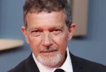 Antonio Banderas aos 65 anos em evento oficial, usando smoking preto e gravata, sorrindo para fotógrafos em tapete vermelho