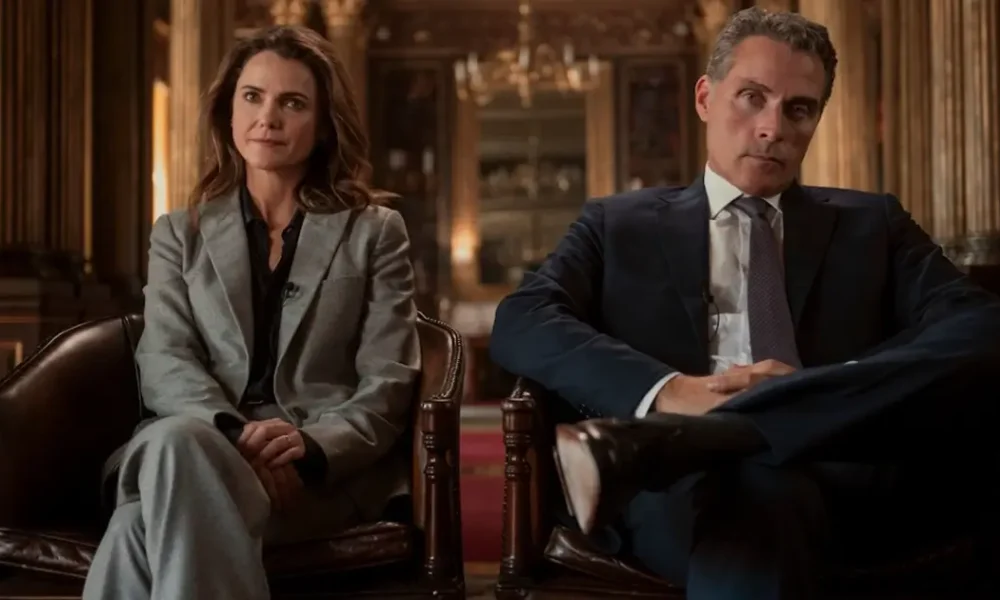 Keri Russell e Rufus Sewell sentados em poltronas formais em cena da terceira temporada de A Diplomata.