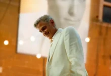 George Clooney em cena do filme Jay Kelly (2025), vestindo terno claro em ambiente interno com iluminação cinematográfica