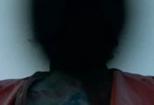 Silhueta sombria de um personagem com jaqueta vermelha em cena enigmática do filme "Para Sempre Minha" (Keeper), dirigido por Osgood Perkins.