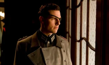 Tom Cruise como Coronel Claus von Stauffenberg em Operação Valquíria - homem de perfil usando uniforme militar cinza com insígnias, óculos e tapa-olho, olhando pensativamente pela janela em ambiente interno com iluminação quente