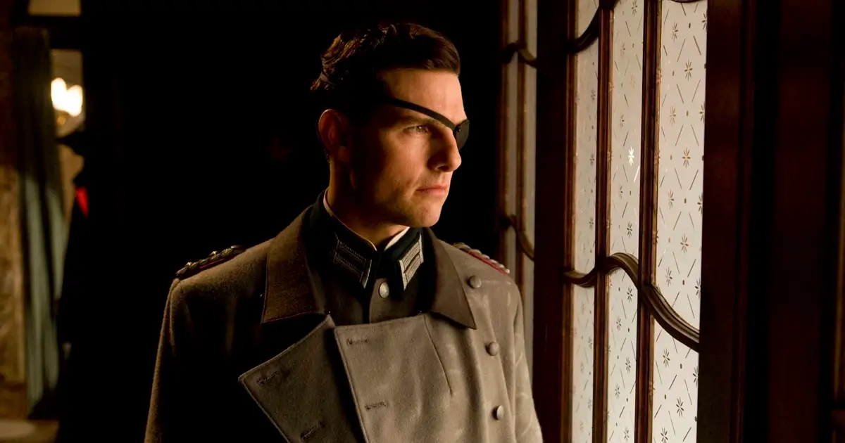 Tom Cruise como Coronel Claus von Stauffenberg em Operação Valquíria - homem de perfil usando uniforme militar cinza com insígnias, óculos e tapa-olho, olhando pensativamente pela janela em ambiente interno com iluminação quente