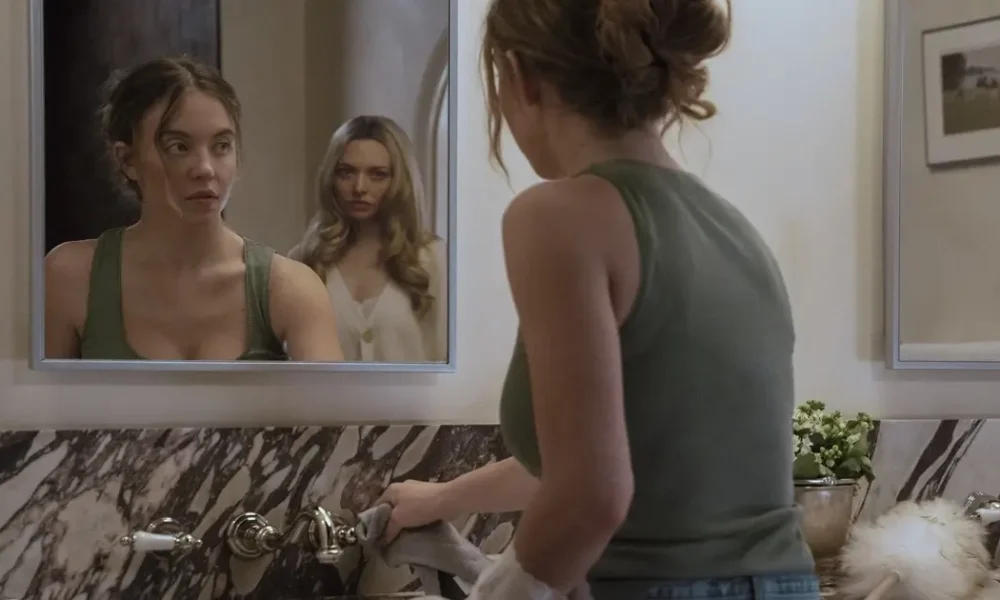 Cena do filme A Empregada (The Housemaid), mostrando a personagem Millie (Sydney Sweeney) diante do espelho em um banheiro luxuoso, enquanto Nina (Amanda Seyfried) aparece refletida ao fundo, criando um clima de tensão e mistério.