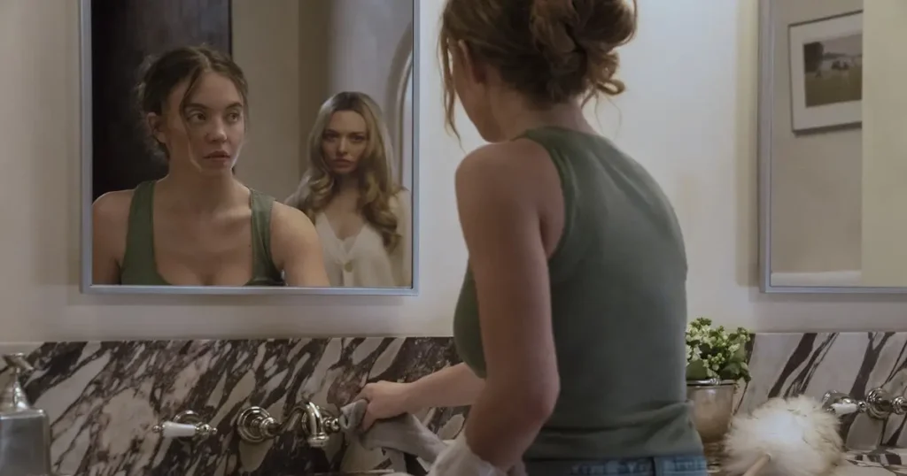Cena do filme A Empregada (The Housemaid), mostrando a personagem Millie (Sydney Sweeney) diante do espelho em um banheiro luxuoso, enquanto Nina (Amanda Seyfried) aparece refletida ao fundo, criando um clima de tensão e mistério.