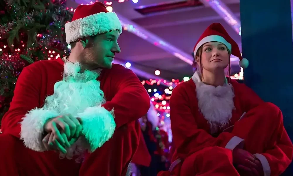feliz assalto 2025 Olivia Holt e Connor Swindells vestidos de Papai Noel em cena do filme Feliz Assalto (Jingle Bell Heist, 2025), da Netflix.